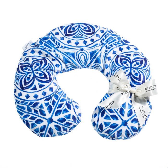A white U-shaped pillow with intricate blue geometric and floral patterns. A ribbon with "Sonoma" printed on it is tied around one arm of the pillow.