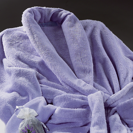 A soft purple bathrobe with a tied belt, displayed against a dark background. A small lavender sachet is placed beside it, adding a touch of elegance and relaxation.