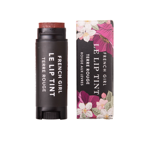 A black tube of FRENCH GIRL Tinted Lip Balm in Terre Rouge stands beside its floral-patterned box, both labeled with the product and brand names in white text.