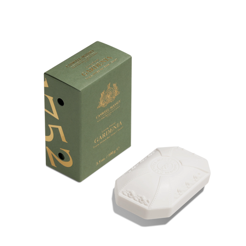A green Caswell-Massey Gardenia Bar Soap box stands next to an embossed, white, oval triple-milled soap with decorative details, both set against a white background.