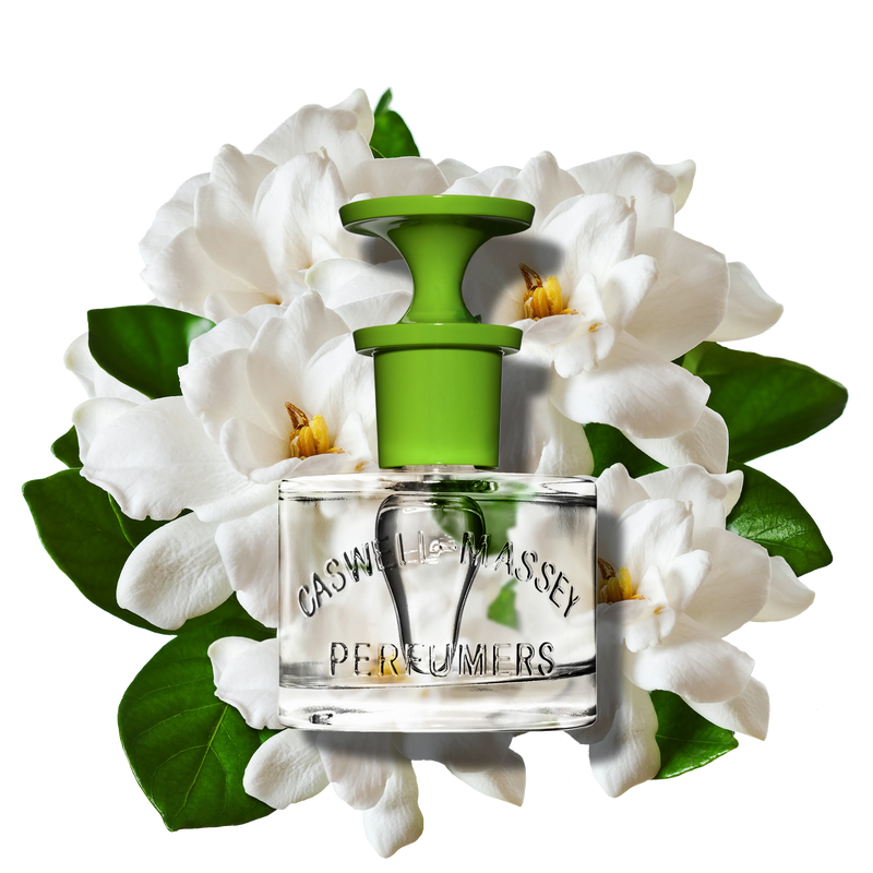 A clear 60ml Caswell Massey Gardenia Eau de Toilette bottle with a green cap, set before white gardenias and green leaves, evokes this elegant floral fragrance with subtle white woods undertones.
