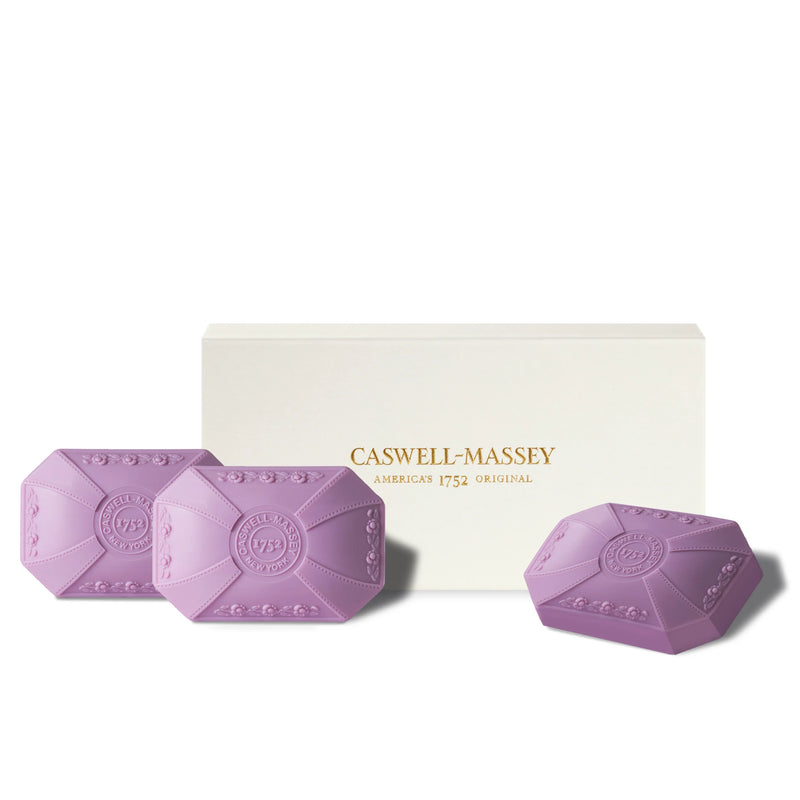 Three lilac Caswell-Massey triple-milled soap bars with decorative embossing in front of their box, which reads "Caswell-Massey America's 1752 Original.