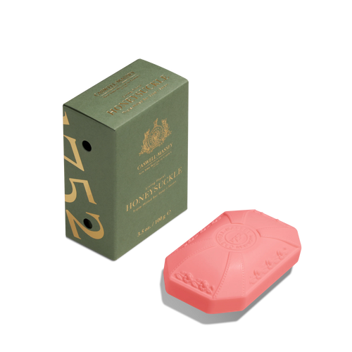 A green Caswell-Massey Honeysuckle box stands beside a pink, octagonal Caswell-Massey Honeysuckle Bar Soap with embossed details, both displayed on a white background.