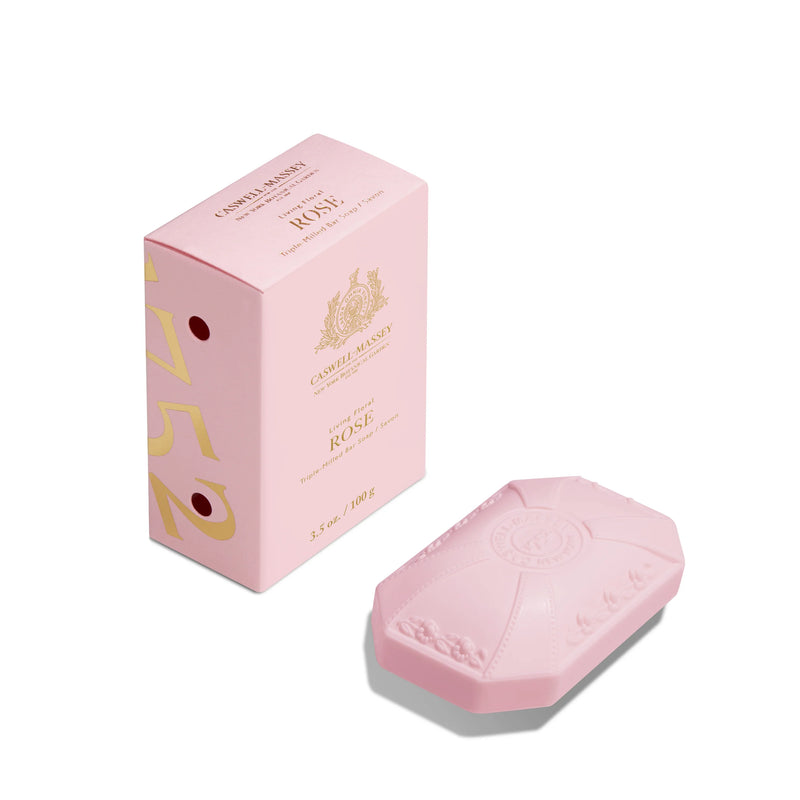 A pink bar of Caswell Massey Rose Luxury Bar Soap 100g with embossed details next to its matching pink and gold packaging box on a white background. The box features elegant gold and white text.