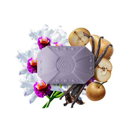 A Caswell-Massey Orchid Bar Soap with embossed text is displayed on a white background, surrounded by white and purple flowers, pear slices, and vanilla beans.
