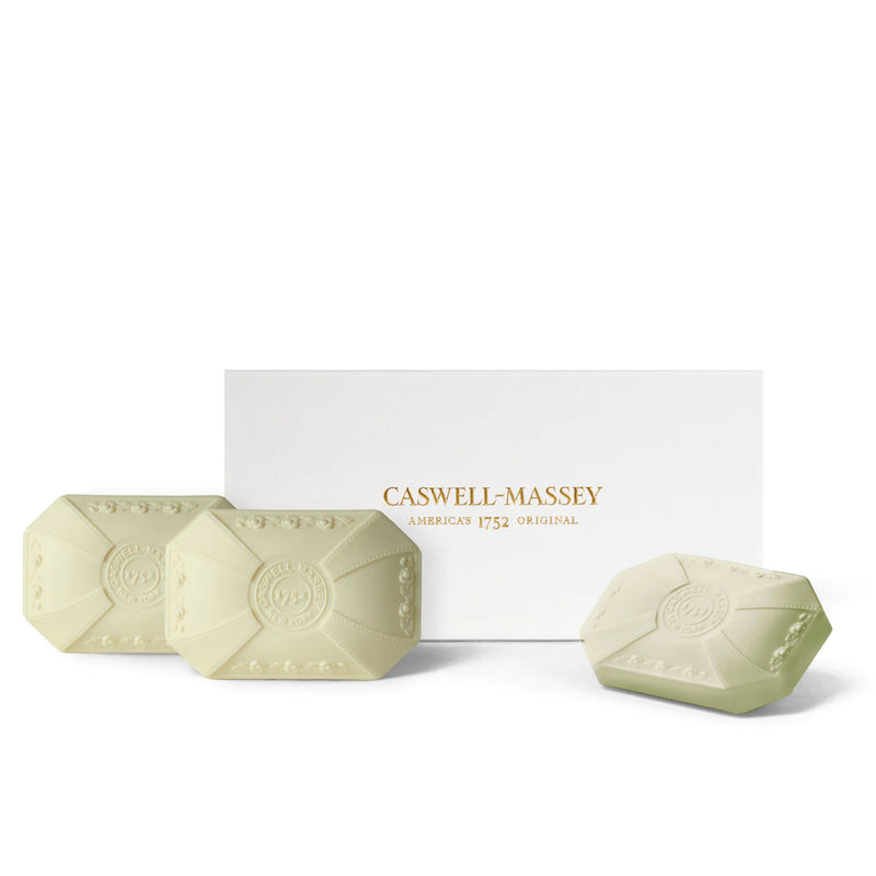 Four light green, hexagonal, triple-milled bath soap bars embossed with a logo, displayed in front of a white Caswell Massey Peony Three-Soap Set box on a plain background.