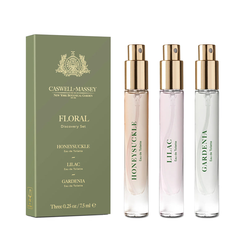Three slender bottles of floral-scented eau de toilettes labeled "honeysuckle," "lilac," and "gardenia" beside their green box labeled Caswell - Massey Floral Discovery Set.