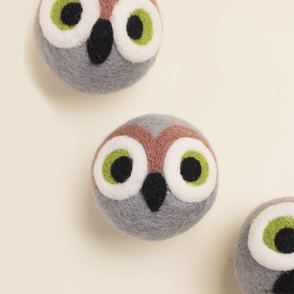The MODERNBEAST - OWL BEASTBALL Wool Dog Toy by MODERNBEAST features three round, gray felt balls resembling owl faces with green and white eyes, brown eyebrows, and black beaks, displayed on a light cream background.