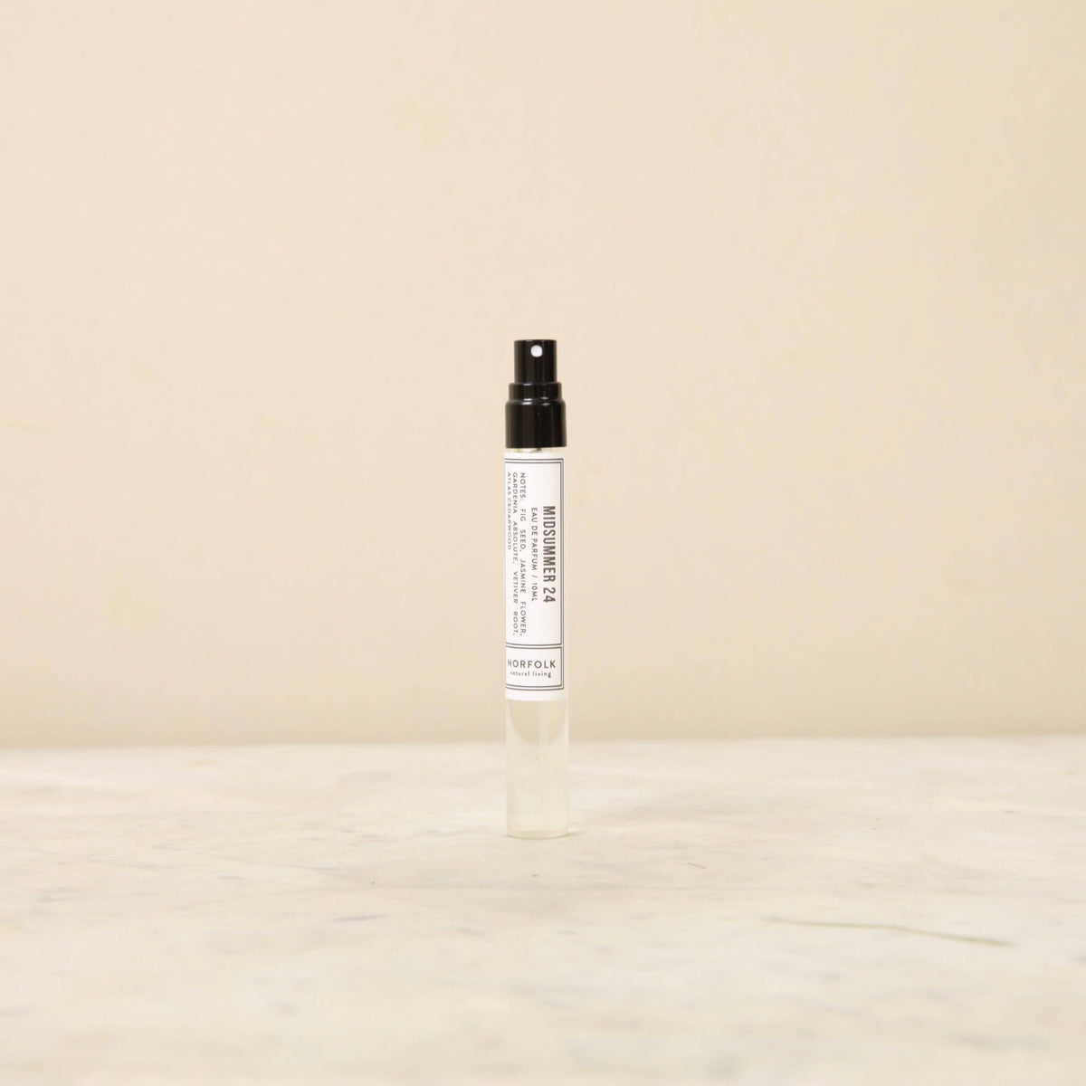 A small, transparent spray bottle with a black cap standing upright on a light beige surface, featuring a white label with minimalistic text and described as containing Norfolk Natural Living Parfum MidWinter 21 - 10ml.