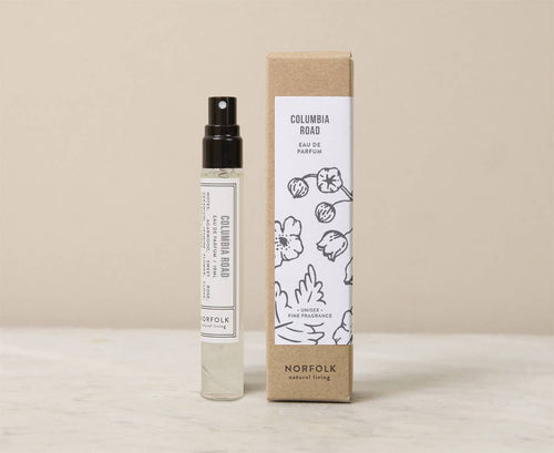 A 10ml glass spray bottle of Norfolk Natural Living Columbia Road Parfum, a vegan floral fragrance inspired by London's flower market, stands beside its beige and white box featuring floral line art and the brand’s logo.