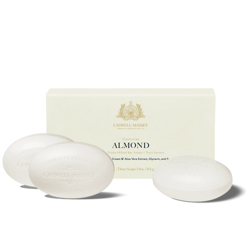 Three oval white bars from the Caswell-Massey Almond Three-Soap Set sit before a cream-colored box with gold accents, showcasing this luxurious triple-milled Caswell-Massey soap enriched with cream and aloe vera extract.