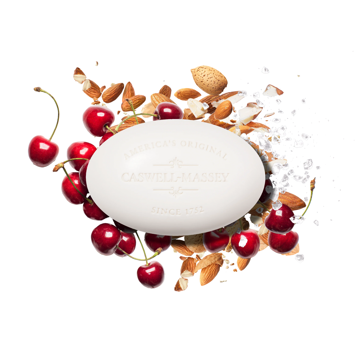 A white oval Caswell Massey Almond Bar Soap is surrounded by fresh cherries, almonds, almond shells, and sea salt on a white background, highlighting the moisturizing lather of this triple-milled soap.