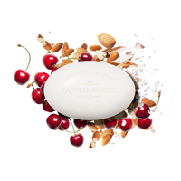 A white oval Caswell Massey Almond Bar Soap is surrounded by fresh cherries, almonds, almond shells, and sea salt on a white background, highlighting the moisturizing lather of this triple-milled soap.