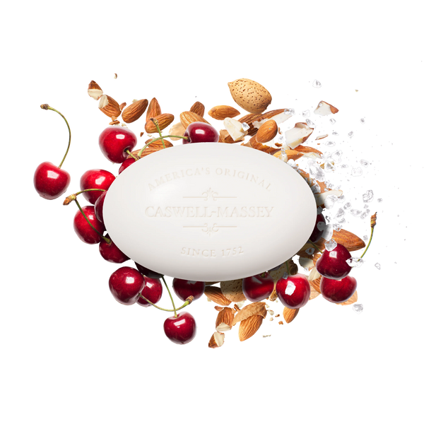 Caswell-Massey Almond Bar Soap, an oval moisturizing soap, is beautifully arranged on a white background with fresh cherries, almond pieces, whole almonds, and scattered white crystals to highlight its luxe appeal.