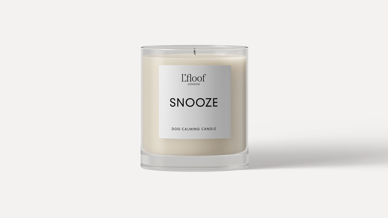 The L'floof Dog Calming Candle SNOOZE, a 330ml essential oil white candle in a clear glass jar, features the “L’floof LONDON SNOOZE DOG CALMING CANDLE” label on a plain white background—ideal for soothing your dog.