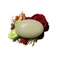 Caswell Massey Ròs Bar Soap, a triple-milled bar with rose and spicy amber fragrance, is shown surrounded by a red rose, sliced lime, green leaves, and brown spice on a white background.