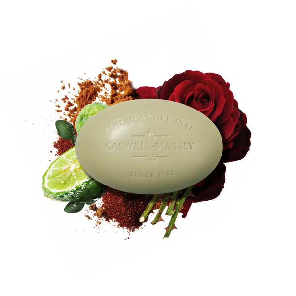 Set against a white background, the Caswell-Massey Ròs Bar Soap is shown with a red rose, sliced lime, leaves, and brown granules, highlighting its triple-milled formula and signature rose and spicy amber fragrance.