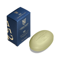 A green oval Caswell Massey Ròs Bar Soap with rose and spicy amber scent sits next to its blue and gold box, featuring the Caswell Massey logo. This triple-milled soap offers a luxurious bathing experience.