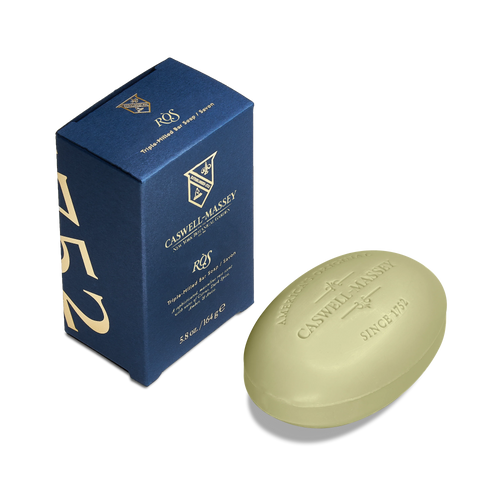 A green oval Caswell Massey Ròs Bar Soap with rose and spicy amber scent sits next to its blue and gold box, featuring the Caswell Massey logo. This triple-milled soap offers a luxurious bathing experience.