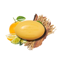 A yellow Caswell Massey Verbena Bar Soap with engraved text sits on wood amid sliced citrus, green leaves, and dried root, highlighting the natural ingredients in this luxurious triple-milled soap.