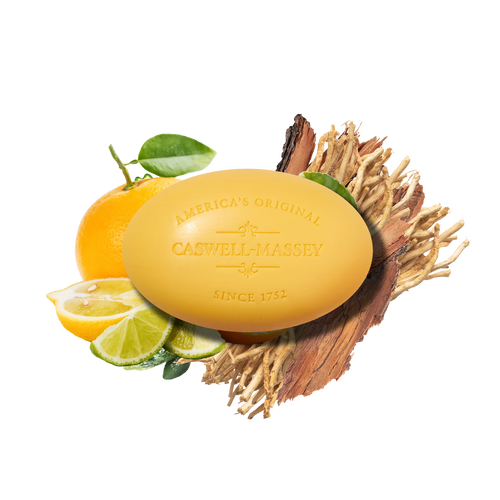 A yellow Caswell Massey Verbena Bar Soap with engraved text sits on wood amid sliced citrus, green leaves, and dried root, highlighting the natural ingredients in this luxurious triple-milled soap.