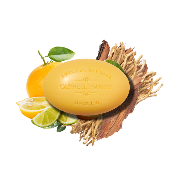 The Caswell-Massey Verbena Bar Soap, a yellow triple-milled soap made with plant-based glycerin, is shown on dried wood with citrus fruits and green leaves, perfect for a refreshing cleanse on a white background.