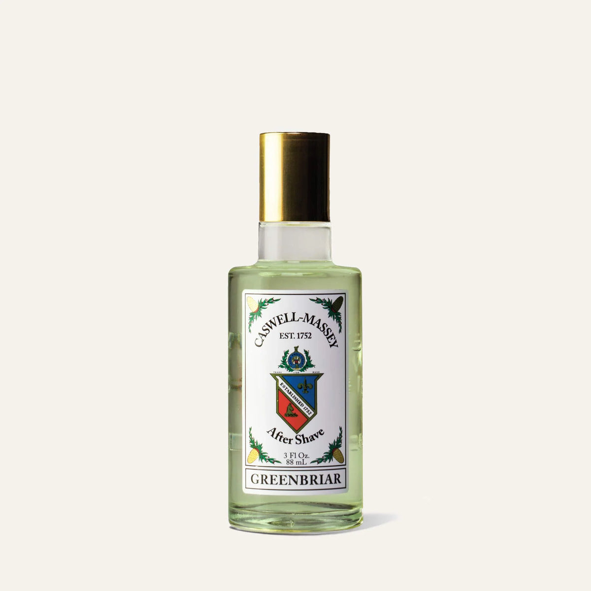 A clear glass bottle of Caswell-Massey Greenbriar Aftershave, a barbershop-inspired tonic with a gold cap and crest-decorated label featuring green accents and text detailing this essential Caswell Massey post-shave ritual.