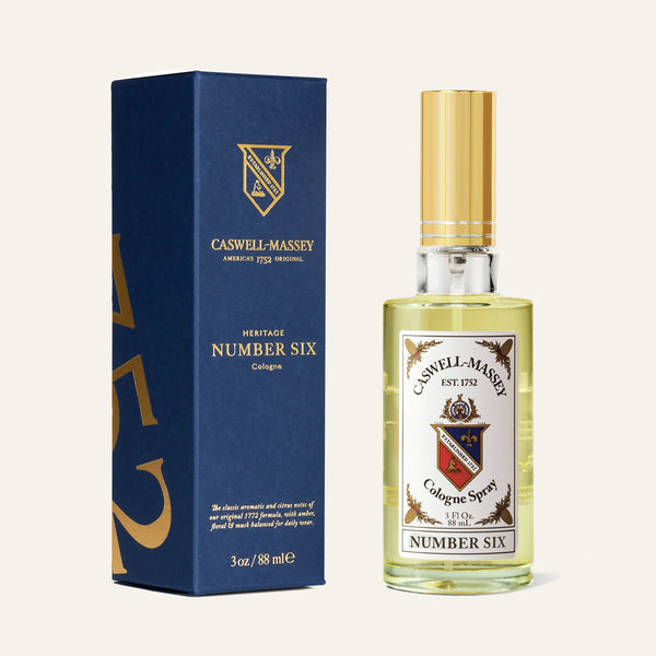 A bottle of Caswell-Massey Number Six Cologne stands beside its blue and gold box. The fragrance offers citrus and woody notes, showcased with a gold cap and a label bearing an elegant crest and text.