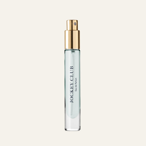 A clear glass spray bottle with a gold nozzle, filled with light blue liquid and labeled "Caswell-Massey Jockey Club Eau De Parfum 7.5mL," a classic men's fragrance, is set against a plain light background.