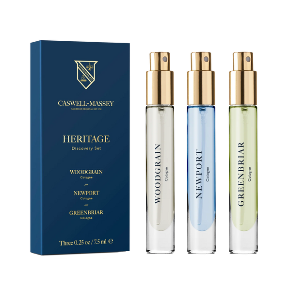 The Caswell-Massey Heritage Cologne Discovery Set includes three glass spray bottles—Woodgrain, Newport, and Greenbriar—with gold caps and colored men's fragrances, all packaged in a blue box.