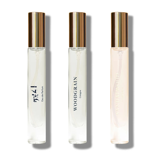 Three clear glass perfume bottles with gold caps are arranged in a row, each labeled "Eau de Parfum," "WOODGRAIN Cologne," and "Sandalwood"—showcasing the Caswell Massey Sandalwood Explorer Discovery Set.