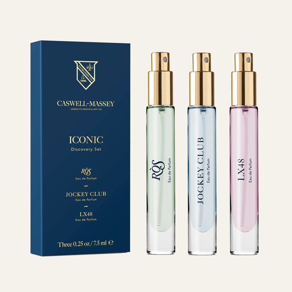 Three Caswell-Massey perfume spray bottles in green, clear, and pink are displayed next to a blue Caswell~Massey Iconic Discovery Set box featuring men's cologne and eau de parfum: RÒS, Jockey Club, and LX48.