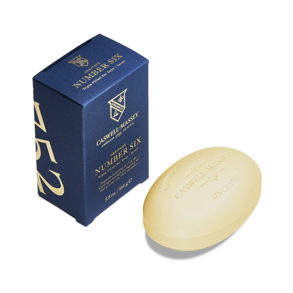 A blue "Caswell-Massey Number Six Bar Soap" box stands next to an oval, beige soap embossed with "Caswell-Massey" and "Since 1752," featuring a refined citrus woody scent, displayed on a white background.