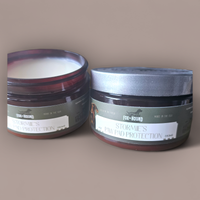 Two round containers of Fox + Hound Stormies Paw Protection - All Season balm by Fox + Hound are displayed, one open showing the cream and one closed with a silver lid, against a plain background.