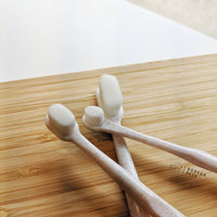 Three white Puppy Polisher Eco Toothbrushes from Wag & Bright Supply Co., featuring medium soft bristles and crafted from wheat straw bioplastic, rest on a light wooden surface. The background is partially blurred, highlighting the "Bodega Pets" logo.