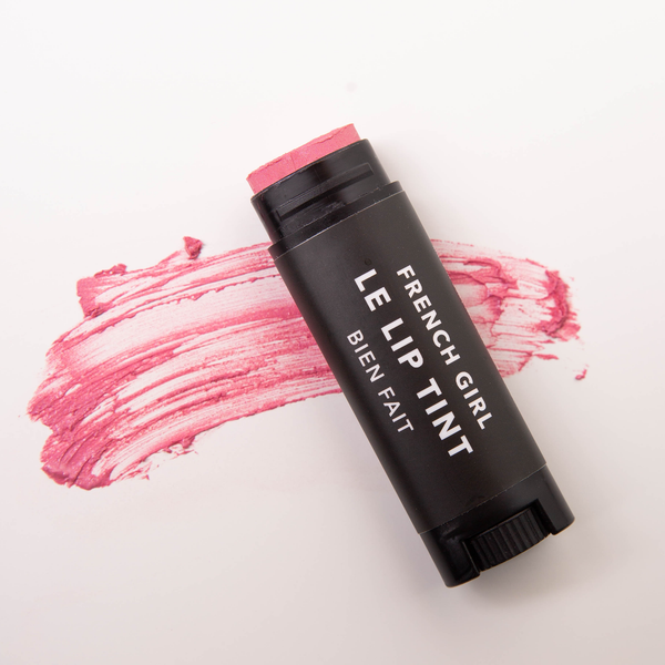 A black tube labeled "FRENCH GIRL Tinted Lip Balm | Bien Fait" rests on a white surface, with a swipe of pink, cruelty-free lip balm smeared behind it.