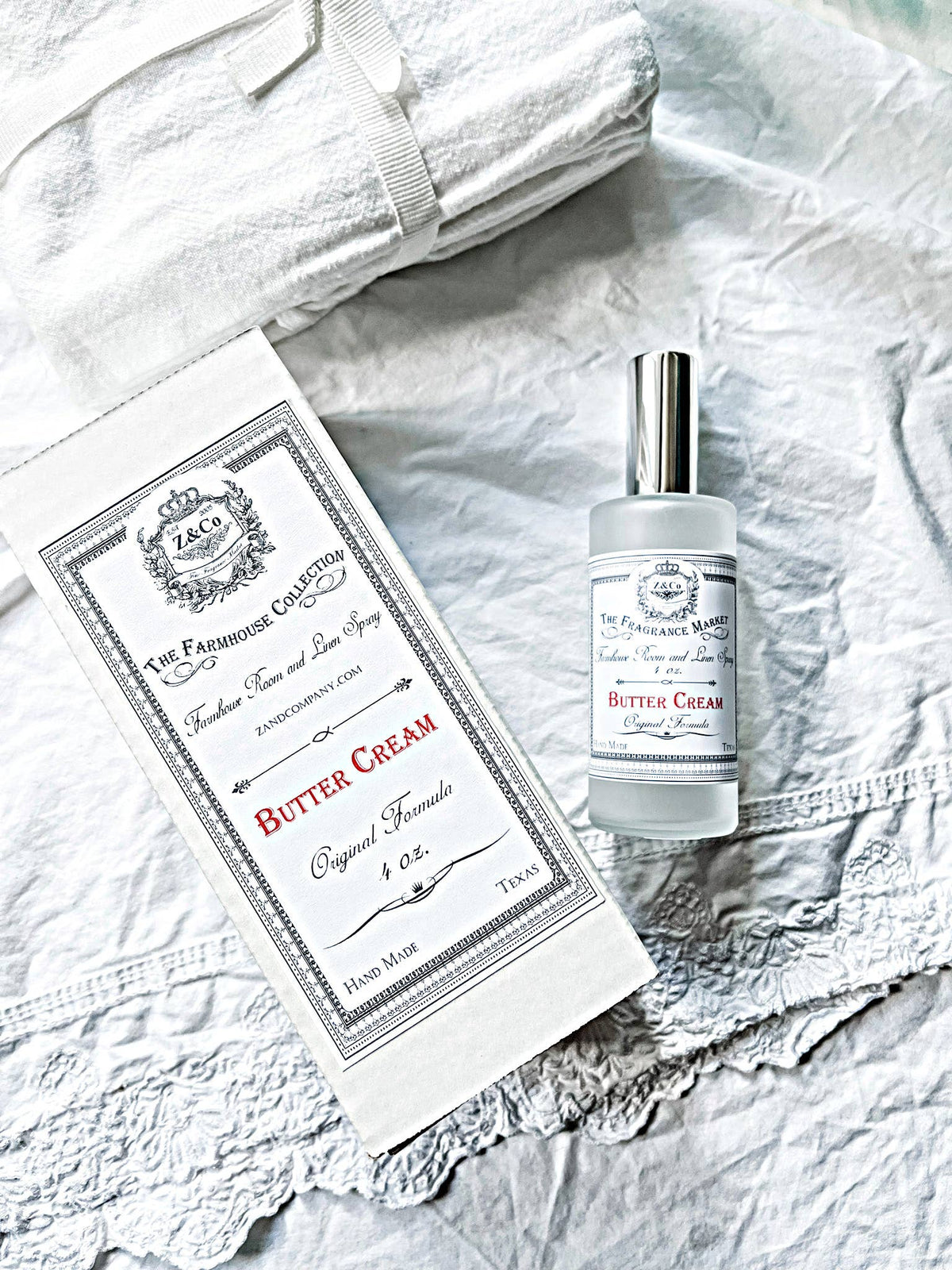 A bottle of Z&Co. Salt Farmhouse Room/Linen Spray by Z&Co. and its box sit on white, textured linens beside a folded towel, creating a clean, bright, and elegant display.