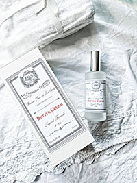 A bottle of Z&Co. Salt Farmhouse Room/Linen Spray by Z&Co. and its box sit on white, textured linens beside a folded towel, creating a clean, bright, and elegant display.
