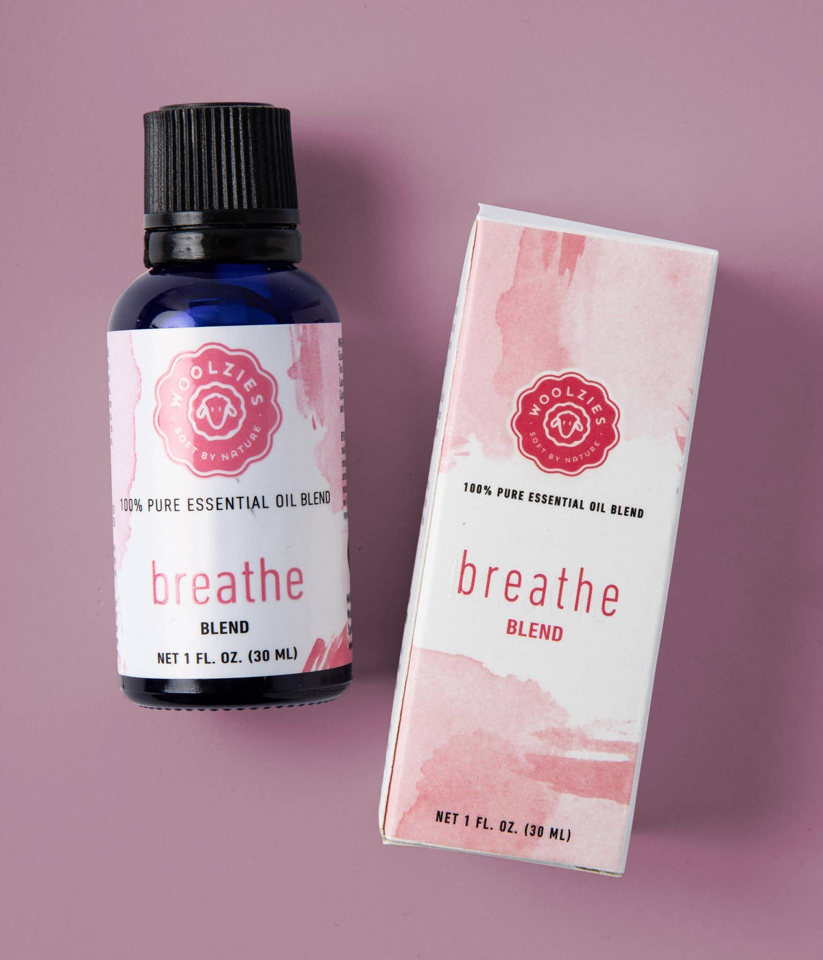 A 1 fl. oz. (30 ml) blue bottle of Woolzies Breathe Blend Essential Oil sits beside its matching box on a mauve surface, both featuring Woolzies branding and ideal for aromatherapy to support respiratory comfort.