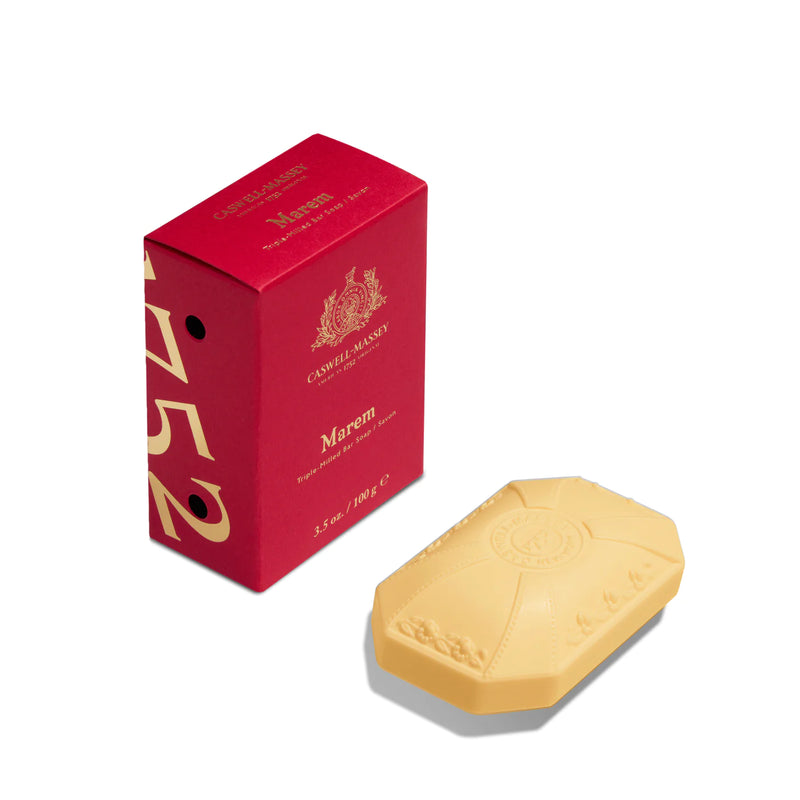 A bar of Caswell Massey Marem Luxury Bar Soap 100gm next to its red packaging box, which has gold text and a crest design. The soap features an embossed emblem on its surface.