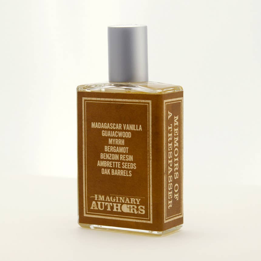 A large bottle of "Memoirs of a Trespasser" fragrance by Imaginary Authors. The rectangular bottle with a silver cap contains amber-colored liquid infused with an adventure scent. Its label lists notes including Madagascar Vanilla, Guaiacwood, Myrrh, Bergamot, Benzoin Resin, Ambrette Seeds, and Oak Barrels.