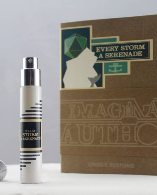 A travel-sized spray bottle of "Imaginary Authors Every Storm a Serenade" is positioned in front of its corresponding box. The packaging, adorned with geometric graphics and text that includes "Imaginary Authors Unisex Perfume," showcases a palette of greens, whites, and browns, capturing the essence of Danish Spruce.