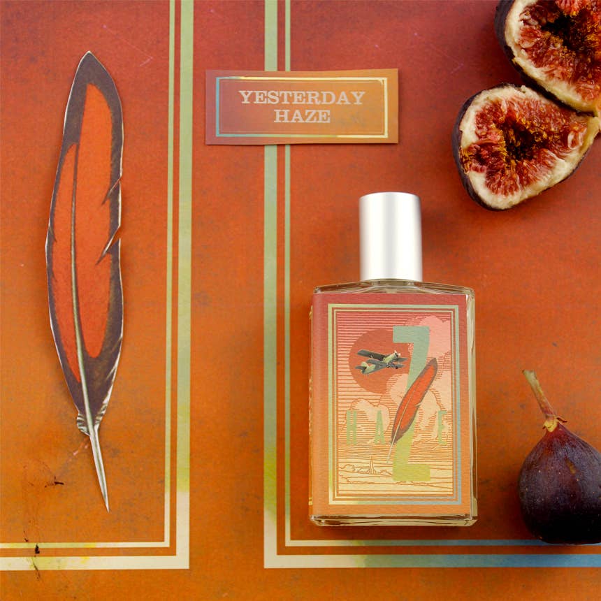 A large-sized bottle of "Imaginary Authors Yesterday Haze" perfume is displayed on a colorful background featuring a feather illustration, sliced figs, and an additional whole fig. The 50ml bottle showcases earthy tones, complemented by a silver cap, exuding a warm and rustic aesthetic. This seductive fragrance offers an inviting allure.