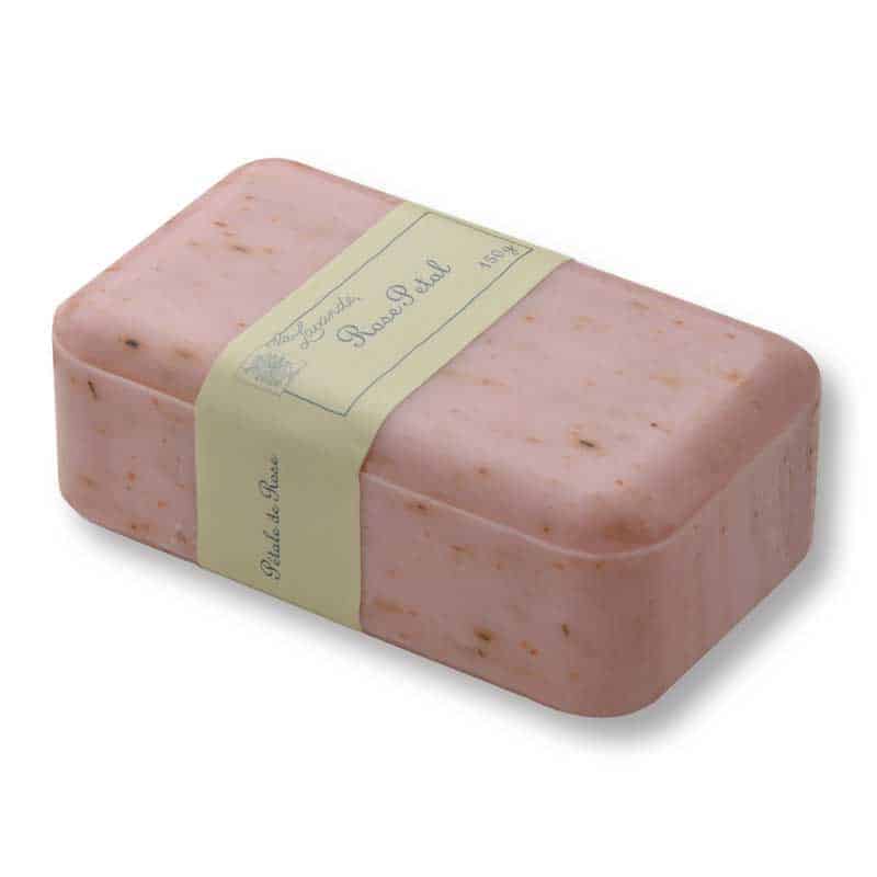 A rectangular bar of pink soap with small brown specks is wrapped in a light-colored label that reads "Savon de Marseille" and "Rose Petal." Featuring the triple milling process, La Lavande Joie de Vivre Rose Petal Hand, Face and Body Soap 150g exudes luxury. The label has decorative French text, set against a white background.