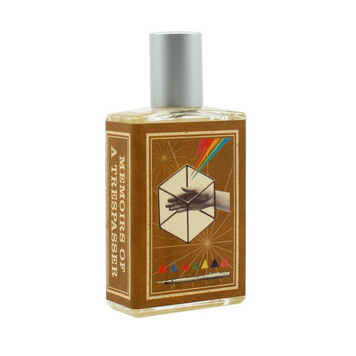 The Imaginary Authors Memoirs of Trespasser - Large Size perfume bottle is a rectangular shape with a silver cap. The label, marked "Memoirs of a Trespasser" from the brand Imaginary Authors, showcases a geometric design featuring a hand reaching inside a cube with colorful lines projecting outward and a row of triangles at the bottom. This adventurous scent contains notes of Madagascar Vanilla, lending it a vintage aesthetic.