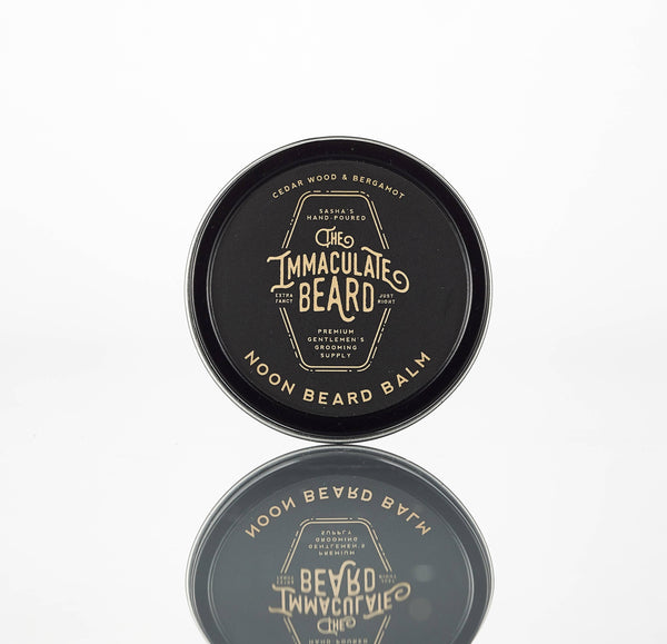 A round black tin of The Immaculate Beard NOON Beard Balm with cedarwood bergamot scent and natural ingredients stands upright on a white background, its reflection visible below.