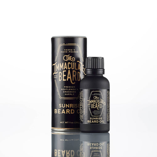 A bottle of The Immaculate Beard SUNRISE Beard Oil by The Immaculate Beard stands before its matching black cylindrical packaging with gold text, both displayed on a white background.