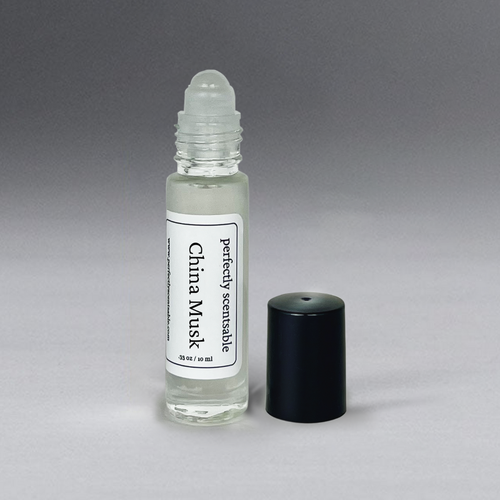 A small glass bottle of Perfectly Scentsable China Musk Perfume Oil - Rollerball is displayed against a gradient gray background. The bottle, boasting a timeless fragrance, has a white label with black text and a black cap that is removed and placed next to it.