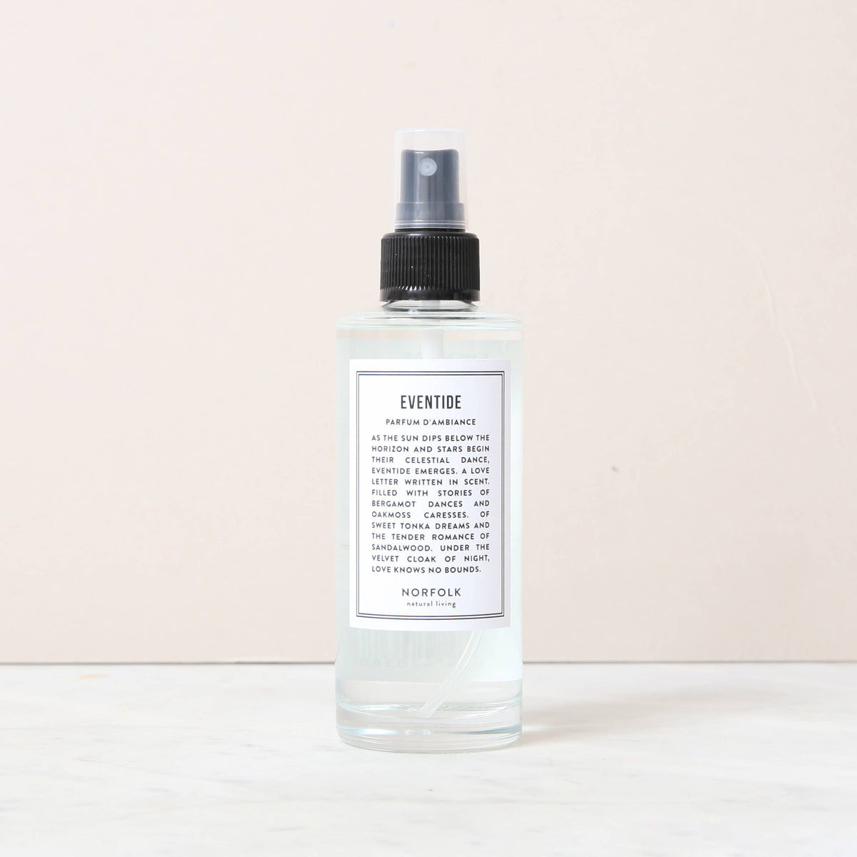 A clear spray bottle labeled "Norfolk Natural Living Eventide Room and Mood Mist," filled with light blue liquid, sits on marble. This natural vegan mist with a black cap and white label adds a fresh touch to any space.