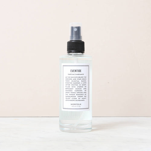 A clear spray bottle labeled "Norfolk Natural Living Eventide Room and Mood Mist," filled with light blue liquid, sits on marble. This natural vegan mist with a black cap and white label adds a fresh touch to any space.